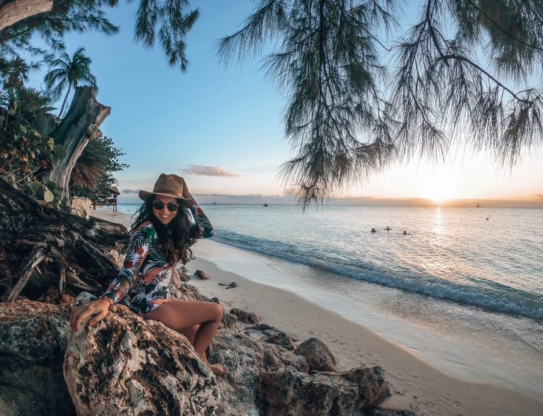 Dani sitting on some rocks, under a tree, close to the shoreline on Seven Mile Beach.