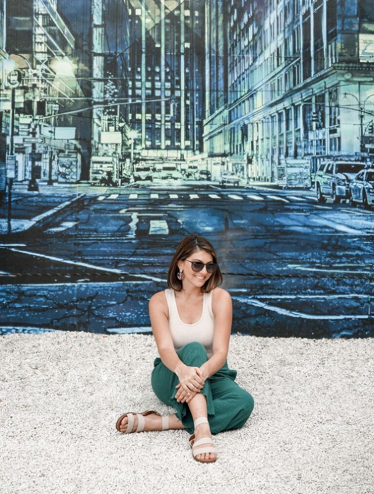 Sitting in front of a painted city scape mural in blue and green hues.