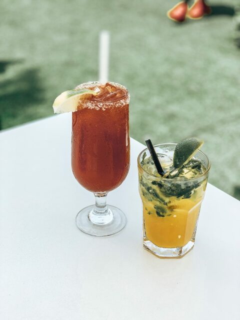 Two pretty cocktails for brunch. A Red michelada, and a brightly colored yellow cocktail garnished with cilantro & a lime.